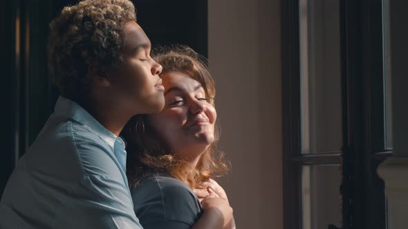 Lesbian Multiethnic Couple Hugging Standing Near Window Indoors alt