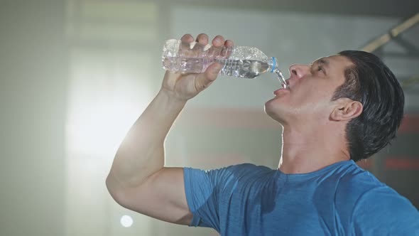 Caucasian young male athlete or sportsman standing in fitness or gym  drinking a bottle of water. alt