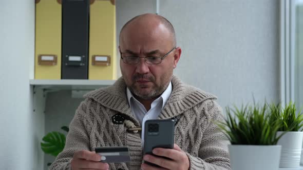Serious Man Wearing Glasses in Warm Sweater Paying with Credit Card Online While Making Orders Via alt