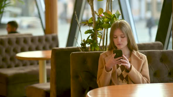 Young girl using smartphones sitting in cafe texting hanging