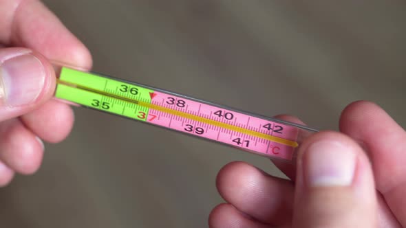 A Medical Thermometer in Men's Hands Close-up. Covid-19 and the Epidemic of Infection