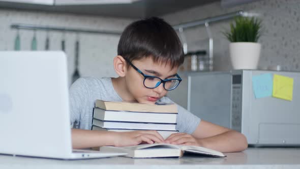 A Child Does Homework By Reading a Textbook with His Head Resting on a Stack of Textbooks. alt