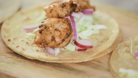 Preparing fresh chipotle shrimp tacos with cotija cheese on a white corn tortillas. alt