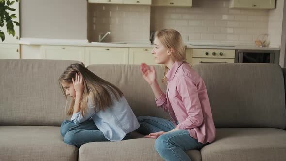 Beautiful Young Mother is Scolding Her Daughter While Sitting on Sofa at Home alt