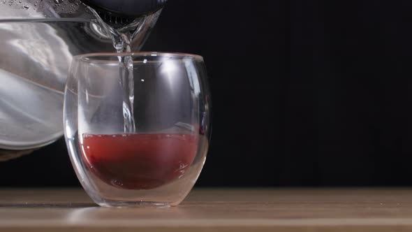 Delicious Healthy Fruit Vitamin Tea in a Transparent Glass is Poured with Hot Water on a Dark alt