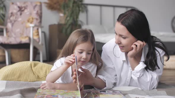 Happy Family Young Mom Reading Book with Child Daughter Laying on Floor at Home alt