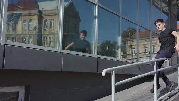 Shot of Casual Guy with Well Clothes Sitting on a Railing in the Street alt