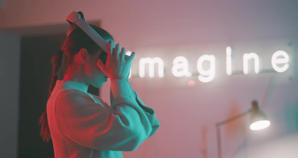 Young woman putting on vr goggles in blue and pink neon lights in side view alt