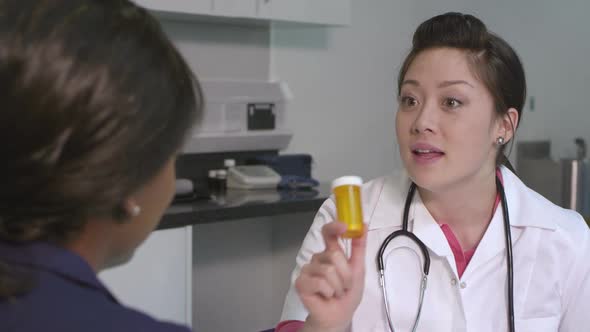 CU Female doctor giving pill bottle to woman talking with her in hospital / London, United Kingdom