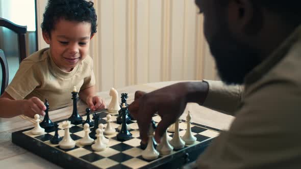 African American boy trying to play chess with his dad