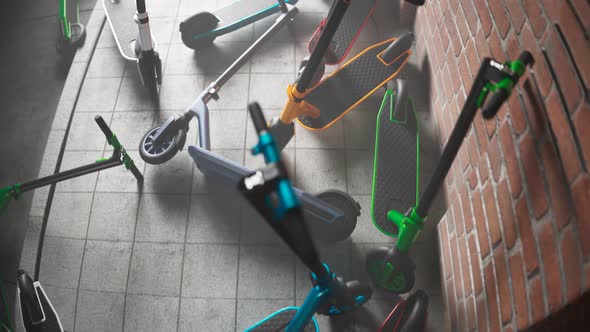 Countless colourful electric scooters left on a sidewalk by a brick wall. 4kHD alt