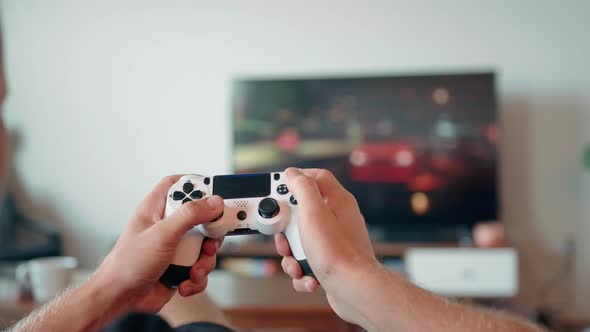 Closeup of the Hands of a Young Man Playing Video Games on a Game Console in Front of a Widescreen alt