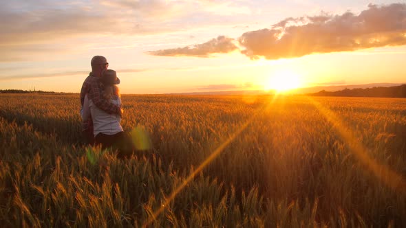 Young caucasian couple  hugging while watching sunset in a barley field