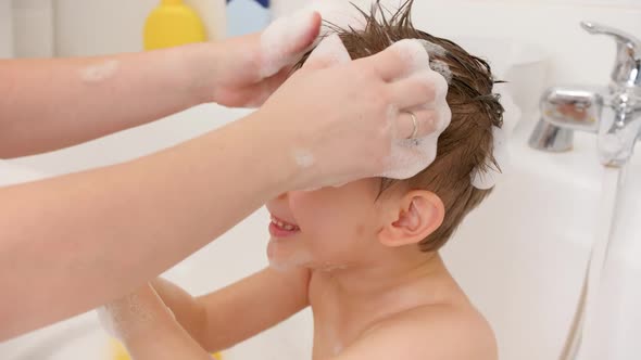 Young Mother Washing Her Little Son in Bath and Making Him Stylish Haircut with Soap Foam alt