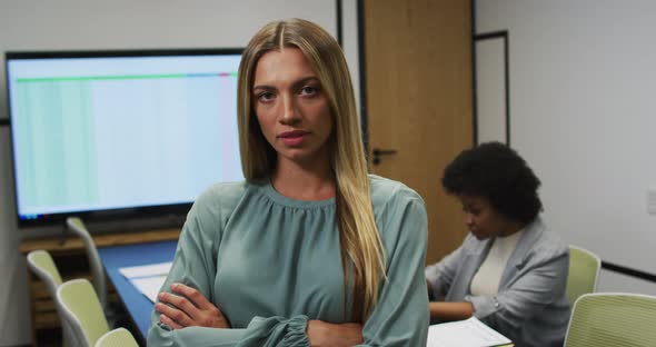 Portrait of caucasian businesswoman smiling in office, with colleague working in background alt