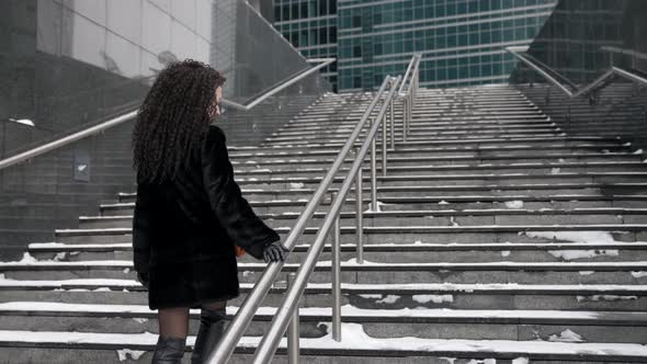 A Curlyhaired Stylish Middleaged Brunette Woman in a Black Fur Coat Walks Alone in the City on a alt
