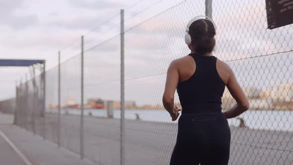 Young Woman In Sportswear And Headphones Jogging Along Harbour alt