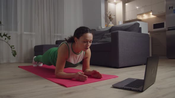 Woman Doing Plank Exercise Watching Video Tutorial on Laptop Indoors alt