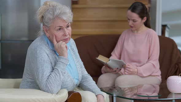 Thoughtful Senior Caucasian Woman with Grey Hair Sitting on Comfortable Armchair in Living Room alt