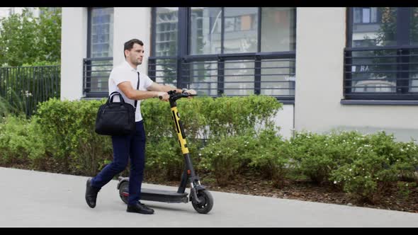 Businessman Rolling Escooter Near on Urban Pavement with Overweight Briefcase alt