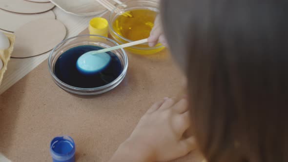 Girl Dipping Easter Egg in Blue Food Coloring alt