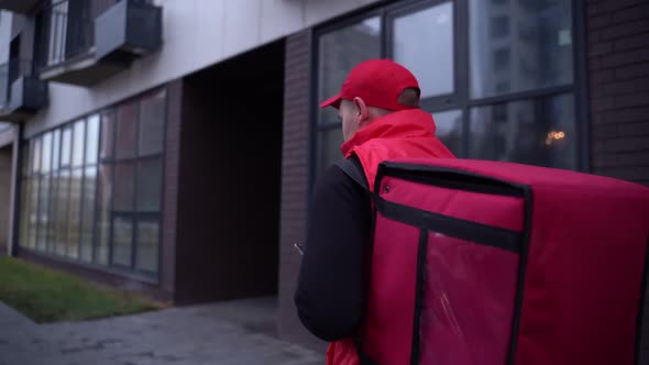 Delivery Guy Wearing Red Uniform While Walking Along Modern Buildings Down City Street with Thermal