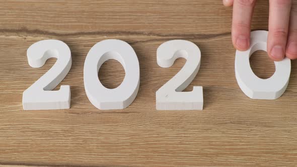 Male hand puts numbers 2020 year, white figures on wooden background, Close up. 4k