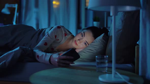 Teenage Girl in Pajamas with Phone in Bed at Night