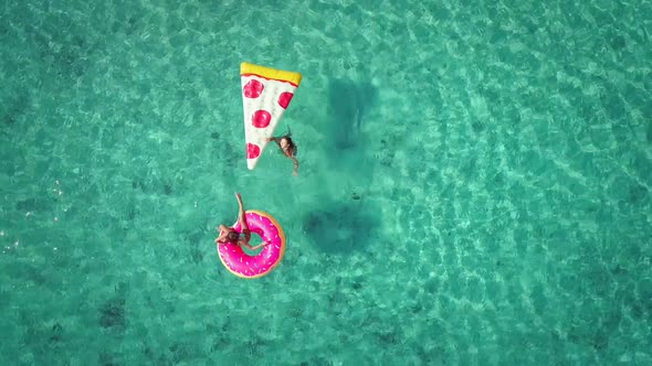 Close aerial view of two young girls swimming and playing in sea with inflatables. alt