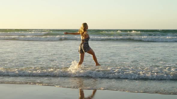 Woman with arms outstretched playing in water at beach alt