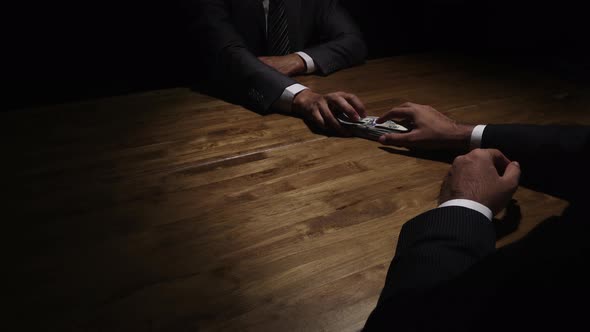 Businessman giving money to his partner on the table in the dark