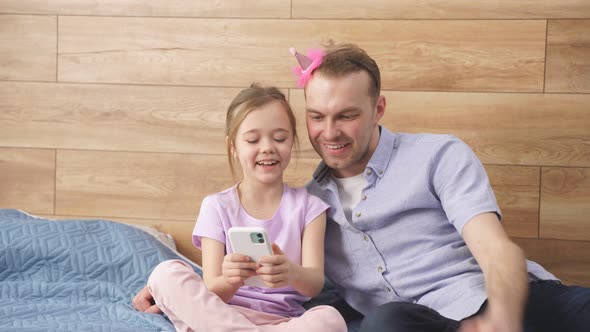 Beautiful Caucasian Child Girl Showing Something Funny on Smartphone to Dad