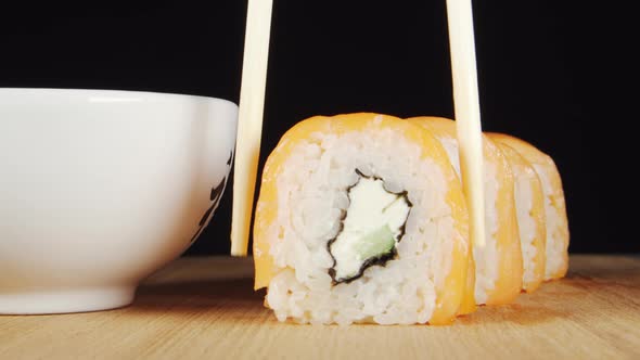 Human hand takes a sushi by chopsticks and dip it in a soy sauce
