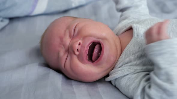 Scared Newborn Girl in Grey Bodysuit Lies on Bed and Screams Out Loudly ...