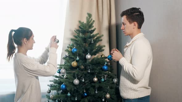 Handsome Young Man and Pretty Lady Decorate Christmas Tree alt