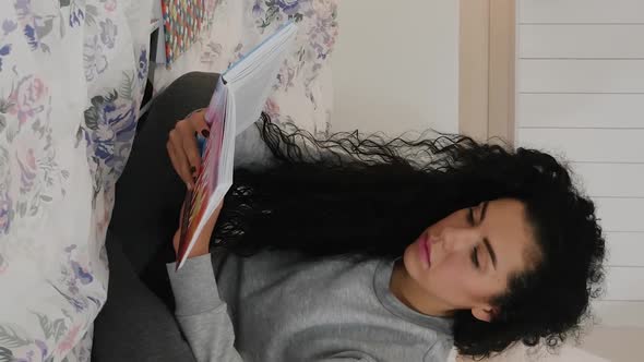 Vertical Video of Cute Young Beautiful Curly Brunette Reading Book in Bed