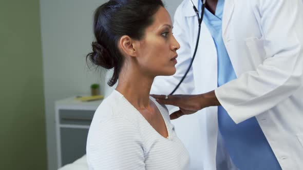Front view of African american male doctor examining female patient in the ward at hospital alt