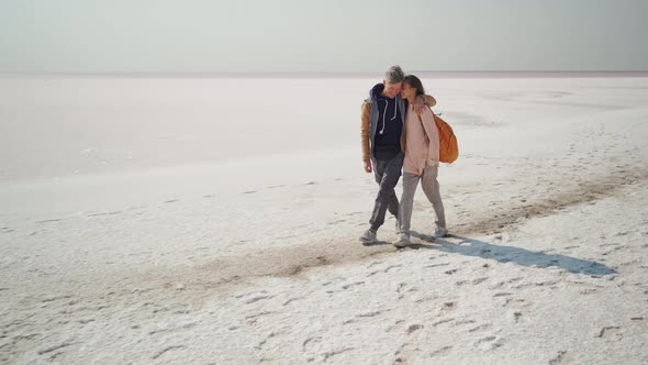 Happy Smiling Lovely Couple Travelers Walking Hugging Each Other on Deserted Pink White Salty Coast alt