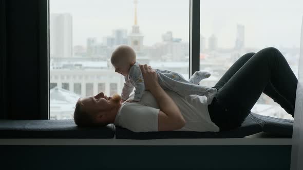 cheerful man with his son lie on the windowsill by the window