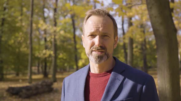 A Middleaged Handsome Caucasian Man Talks to the Camera with a Smile in a Park in Fall  Closeup