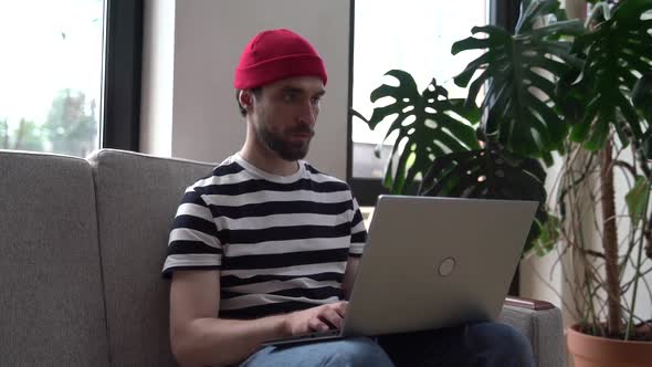 Modern, young man working on a laptop, sitting on a sofa in a cafe or at home alt