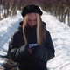Young Long Haired Blonde in Beret and Black Jacket Uses Mobile Phone on Winter Walk - VideoHive Item for Sale