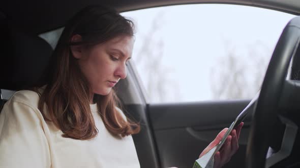 Young Female Driver Holds a Map in Her Hands and Chooses the Direction for the Trip