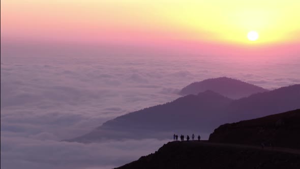 Tourist Silhouettes on Hill Top Against Foggy Mountains