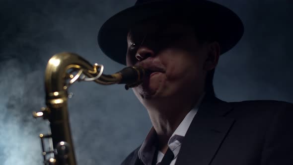 Man saxophonist in a hat and suit plays the saxophone in a smoky studio. alt