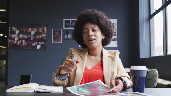Mixed race businesswoman sitting having a video chat going through paperwork in a modern office alt
