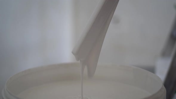 Mans Hands Mixing a Gallon of White Paint with Wooden Paint Stirring Stick Sitting on Floor Closeup alt