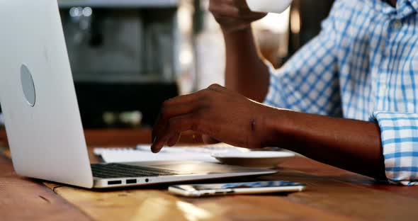 Man using a laptop while having cup of coffee alt