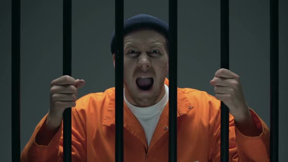 Aggressive Dangerous Male Prisoner With Scar on Face Holding Bars and Shouting alt