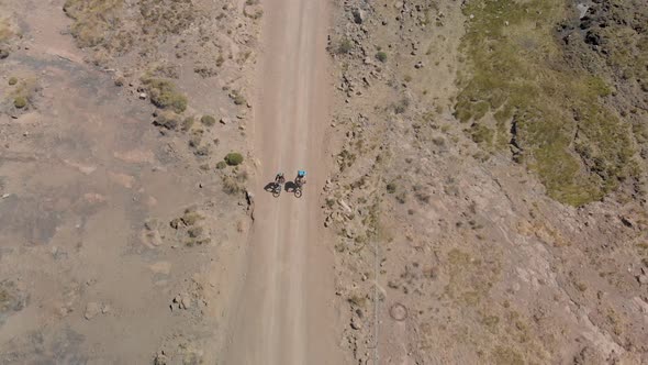 aerial shot following two mountain bikers climbing up a gravel road mountain pass alt